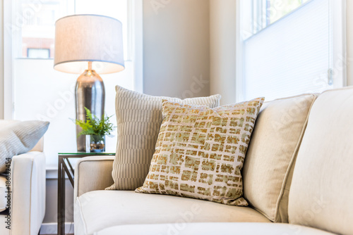 Closeup of two pillows on couch or sofa by bright window in modern apartment, house or home with staging of large beige, neutral white colors, lamp photo