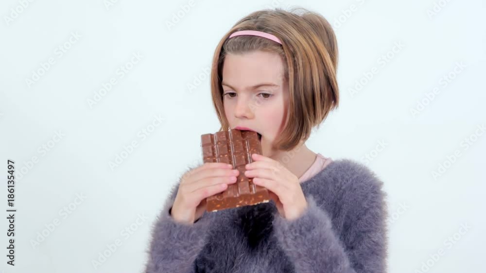 A small girl is eating a chocolate with rice and she doesn't like it. A small girl is eating a chocolate with rice and she doesn't like it.