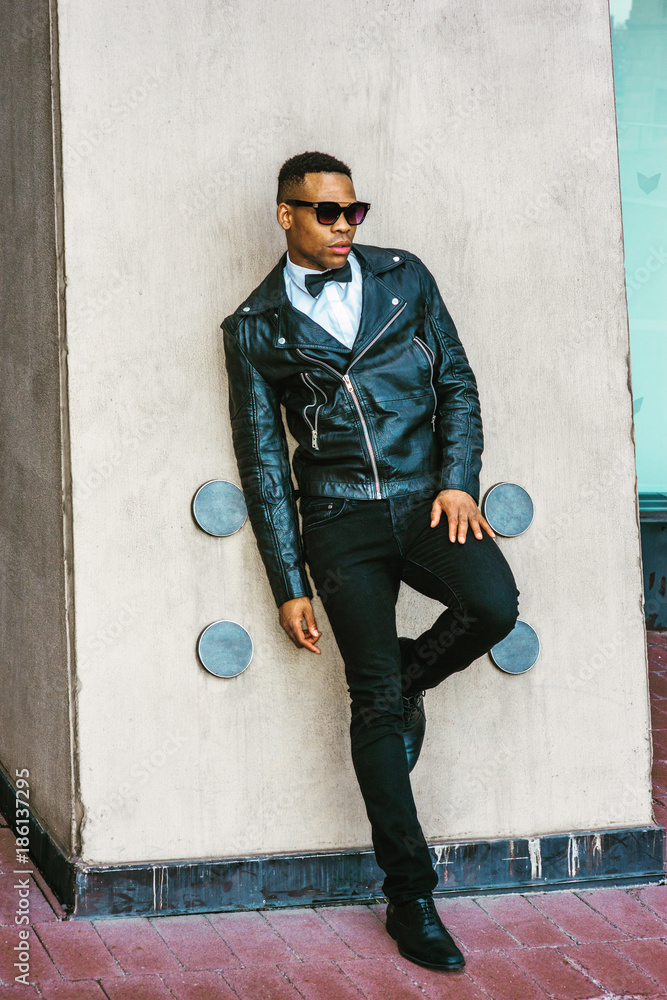 Man Urban Autumn/Spring Casual Fashion. Wearing black leather jacket, white  undershirt, black bow tie, jeans, sunglasses, African American guy standing  against wall on street in New York.. Stock Photo | Adobe Stock