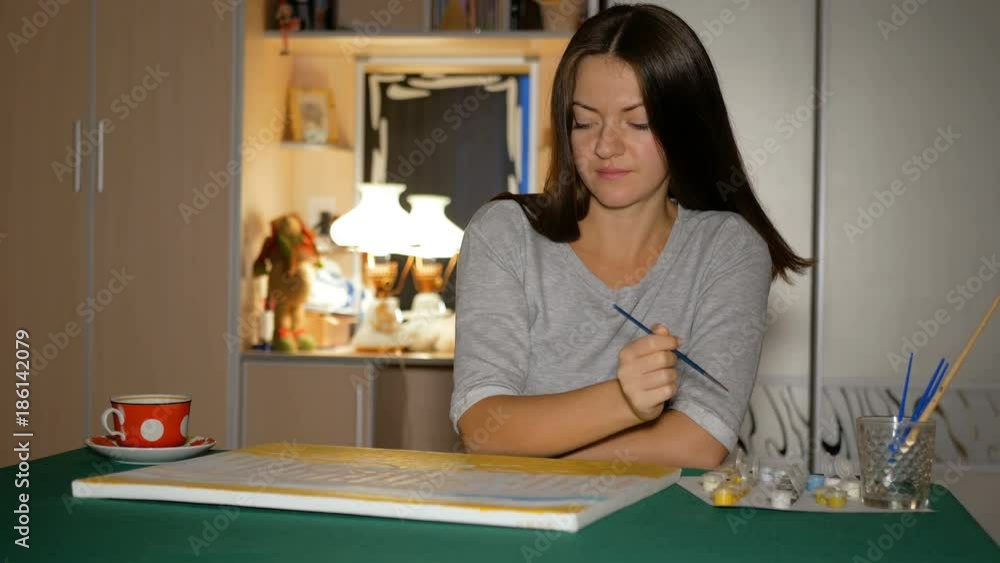 The beginning artist paints her first big picture at home on the table. Girl takes her hands a clean brush and chooses paint. The beginning artist paints her first big picture at home on the table. Girl takes her hands a clean brush and chooses paint.