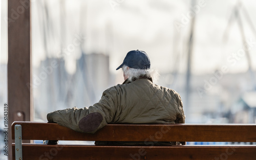 Jubilado sentado en un banco del puerto al sol al atardecer