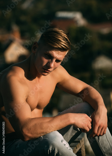Man sportsman with muscular torso sit on natural landscape