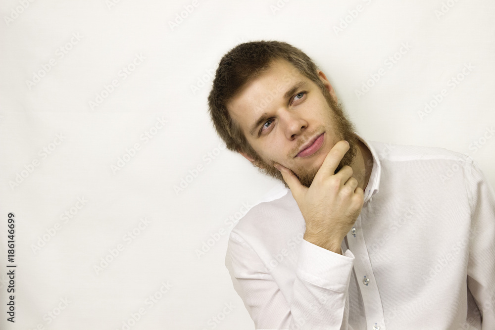 young man sits thoughtfully on a white background in a white shirt with a beard. young man sits thoughtfully on a white background in a white shirt with a beard.