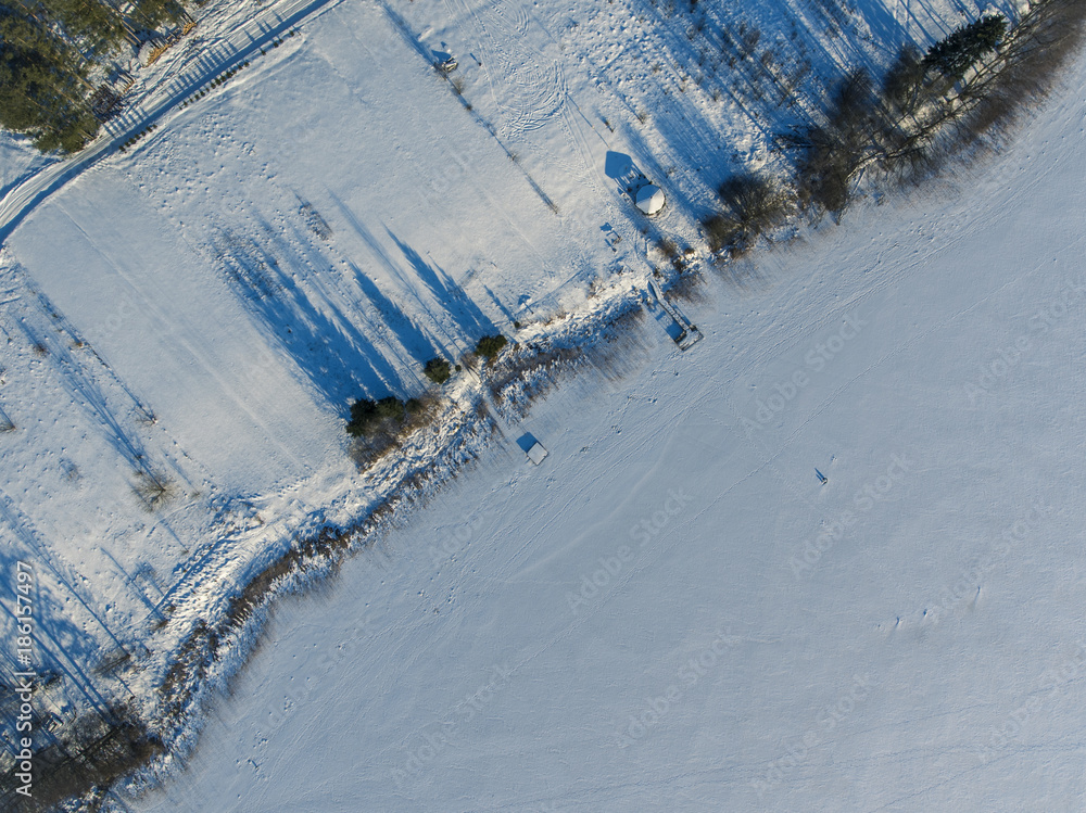 Obraz premium Aerial view over frozen lake cover in white snow with long blue shadows from trees in Latazeris, Lithuania. During cold winter day.