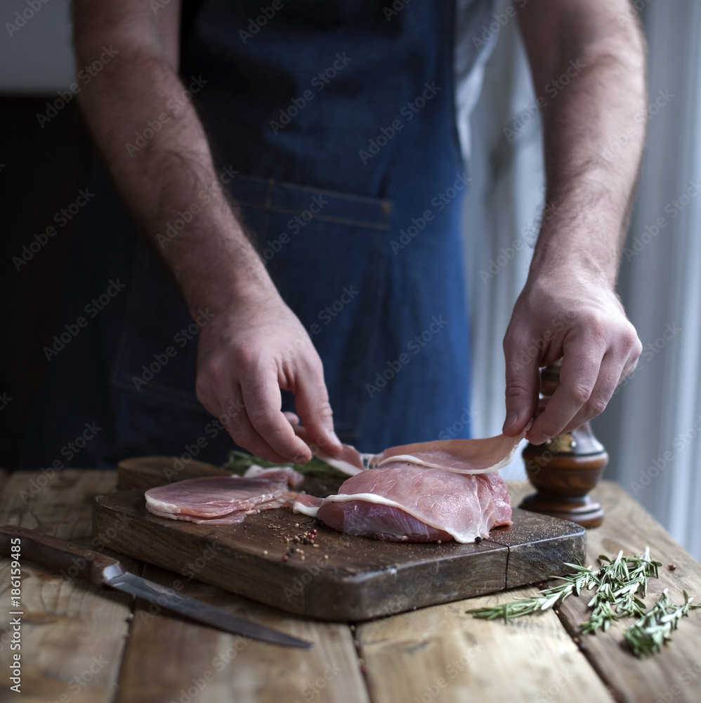 man in kitchen apron holds meat in hands, wooden table and spices