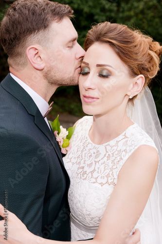 Close-up portrait of a lovely loving couple kissing newlyweds on a background of summer greenery