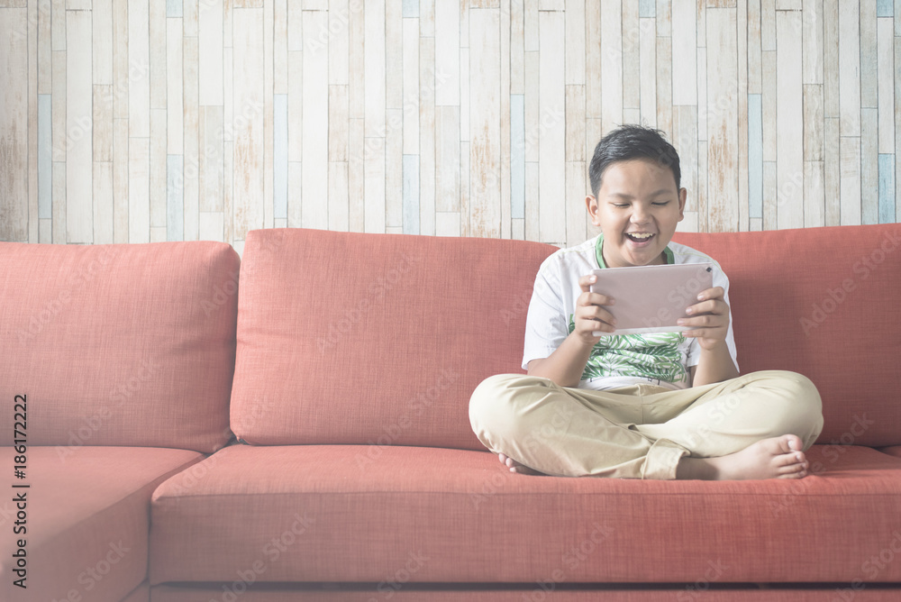 young asian boy using digital tablet on a sofa at home sitting cross-legged. boy relaxing on sofa at home. technology / IT concept. Computer learning concept . young asian boy using digital tablet on a sofa at home sitting cross-legged. boy relaxing on sofa at home. technology / IT concept. Computer learning concept .