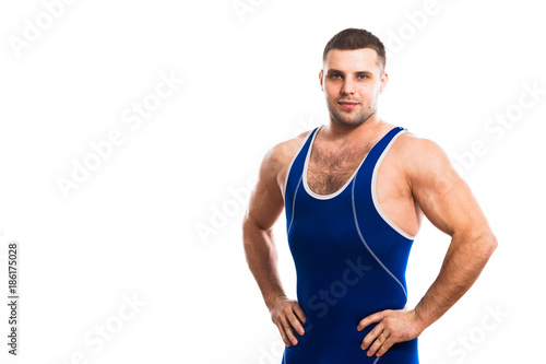 A young dark-haired man fighting Greco-Rican wrestling, a master of sports in grappling in a blue wrestling tights smiling and holding his hands at the waist against a white isolated background