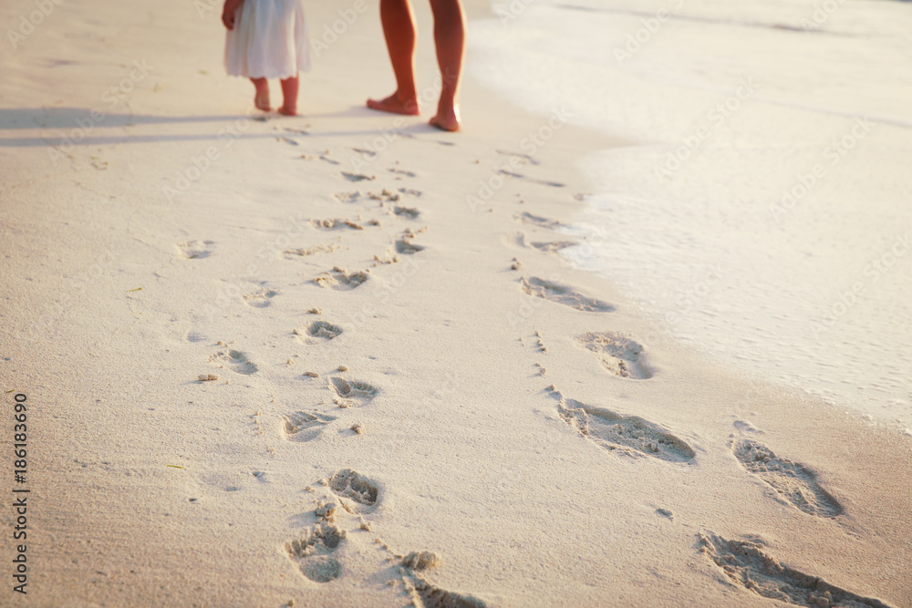 mother and daughter walking on beach leaving footprint in sand
