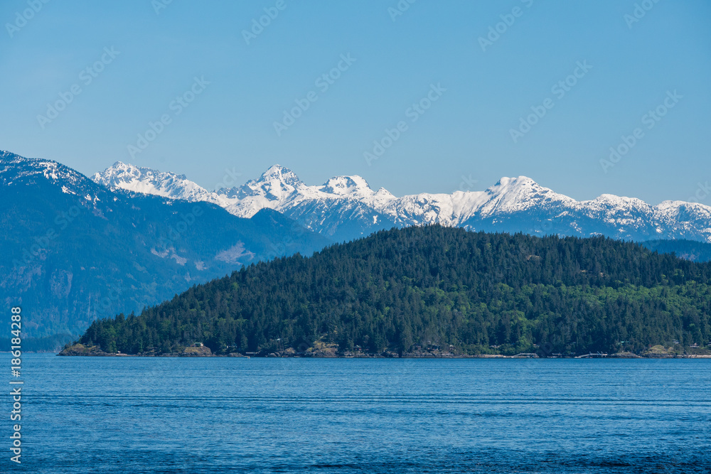 layered mountain range besides ocean under the blue sunny sky