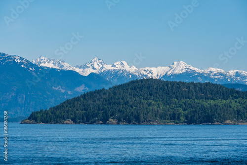 layered mountain range besides ocean under the blue sunny sky
