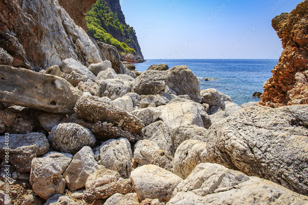 Rocky and stony shore of tropical sea. view of sea through stones of coastline. Mountains and sea. Seascape on hot, sunny summer day. Turkish nature. Rocky and stony shore of tropical sea. view of sea through stones of coastline. Mountains and sea. Seascape on hot, sunny summer day. Turkish nature.