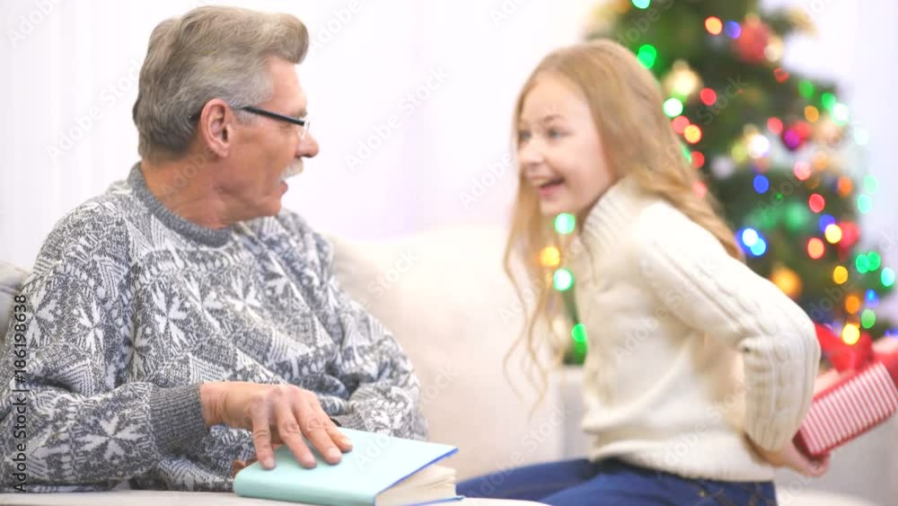 The old man read a book and take a gift from a girl near the christmas tree The old man read a book and take a gift from a girl near the christmas tree