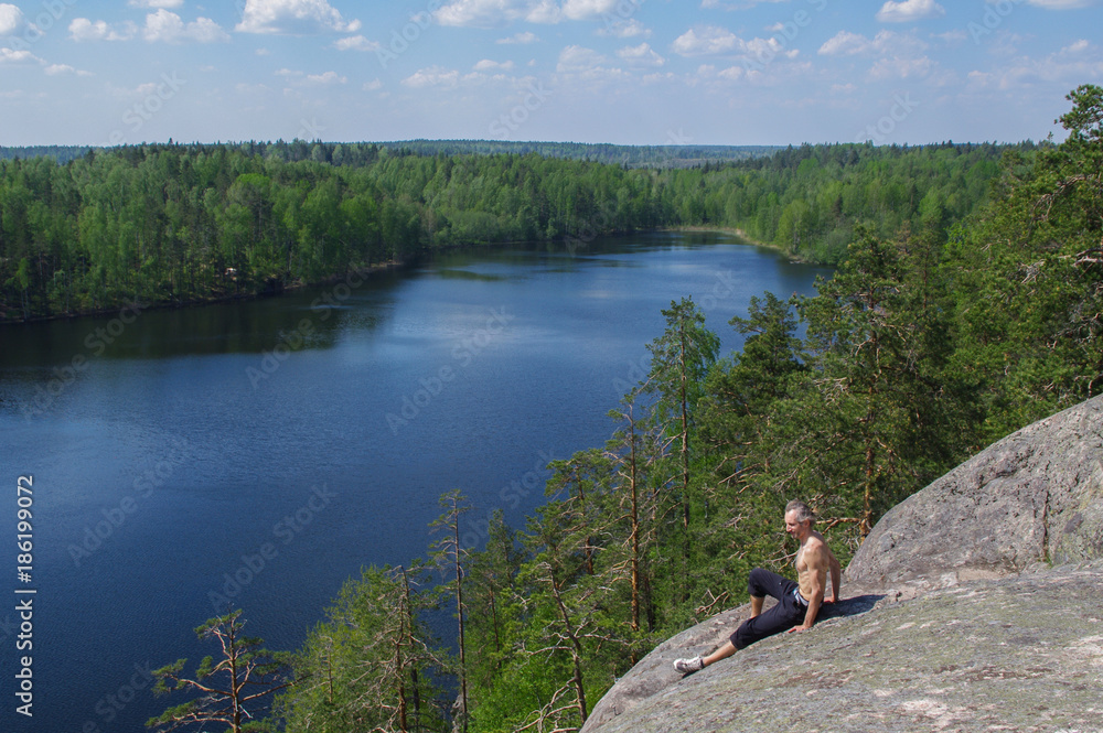 Fototapeta premium man sitting on cliff relaxing, above the lake Yastrebinoye, Priozersky district, Leningrad region, Russia