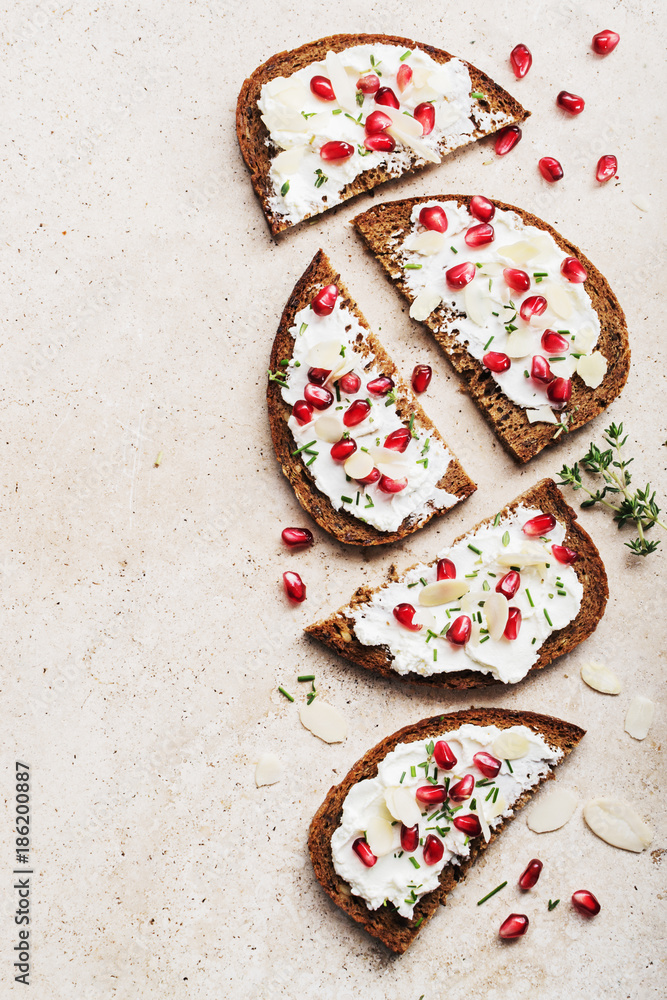 Open sandwiches rye bread with cream cheese and pomegranate seeds, flakes of almond on marble surface. Healthy snack concept. Top view. Open sandwiches rye bread with cream cheese and pomegranate seeds, flakes of almond on marble surface. Healthy snack concept. Top view.