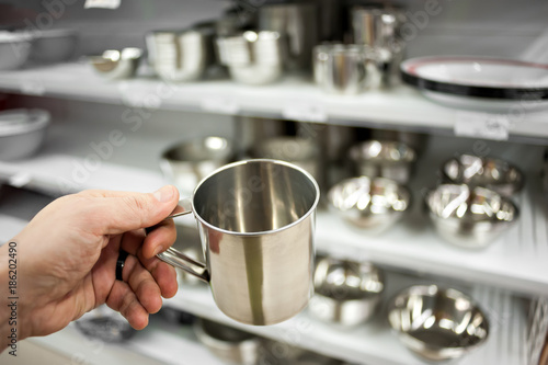 The buyer s hand of a man with a steel bowl on the background of a rack with utensils made of steel
