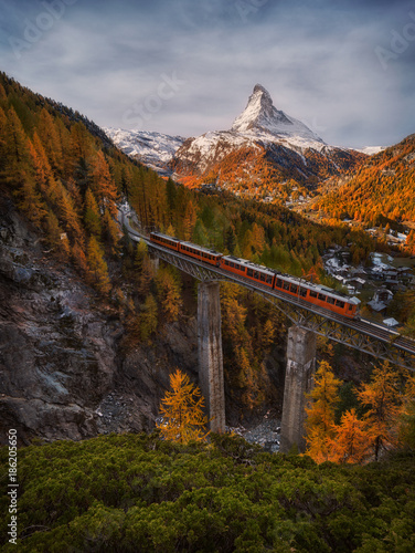 Scenic autumn view on snowy Matterhorn peak with blue cloudy sky , bridge and Gornergrat tourist train in Zermnatt, Switzerland.