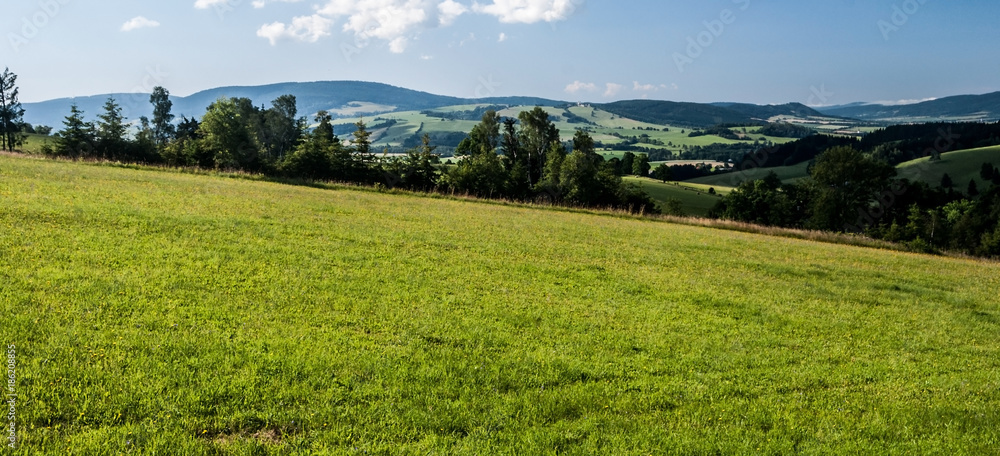 Obraz premium mountain countryside with meadows, fields, villages, trees, hills and blue sky with clouds