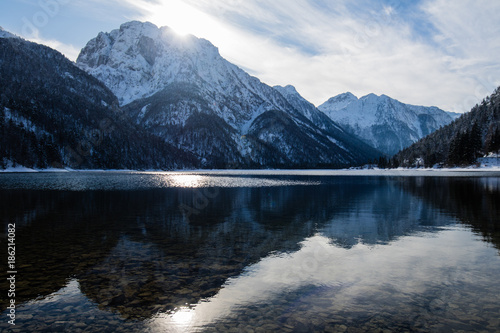 alpine mountain pass winter scenery landscape by lake lago del predil in sunny blue sky in snowfall, italy photo