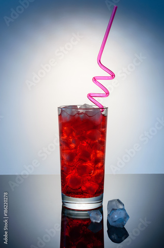 red drink in glass with red straw and ice cubes photo