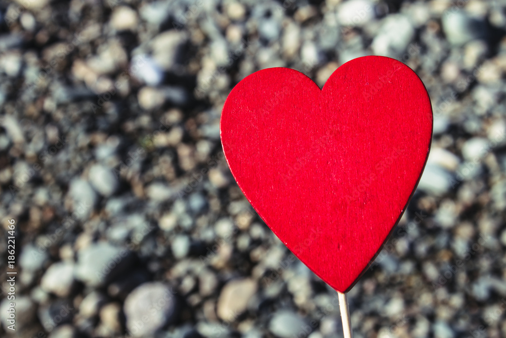 A man holds a red wooden heart on a stick against the background of nature, sky, stones. The concept of Valentine's Day. A man holds a red wooden heart on a stick against the background of nature, sky, stones. The concept of Valentine's Day.