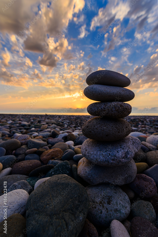 Stones pyramid on sand symbolizing zen, harmony, balance. Black sea at sunset in the background.