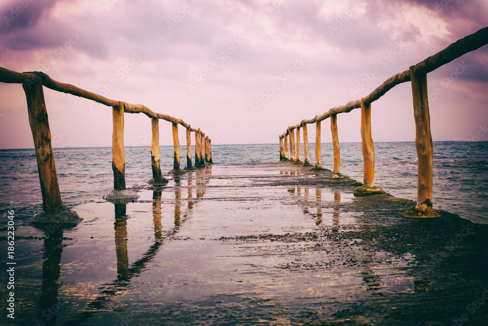Perspective view of a pier on the seashore with clear blue sea and dramatic sky