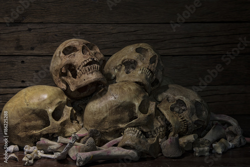 Human skulls and pile of bones are laid on old wooden floors and background on a night where the atmosphere is scary and dim  lights. Halloween night, Life and death concept. Still life style, art.
