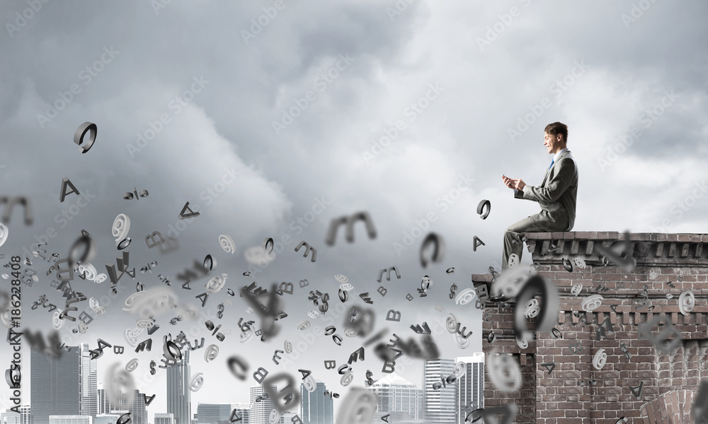 Man on roof edge send message with smartphone and symbols flying around Man on roof edge send message with smartphone and symbols flying around