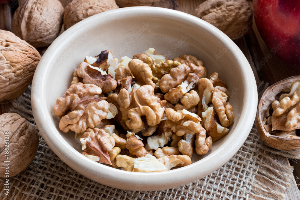 Shelled walnuts in a bowl, with whole walnuts in the background Shelled walnuts in a bowl, with whole walnuts in the background