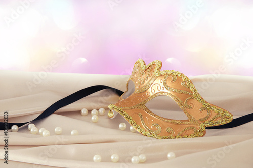 Image of elegant gold venetian mask over delicate silk fabric background.