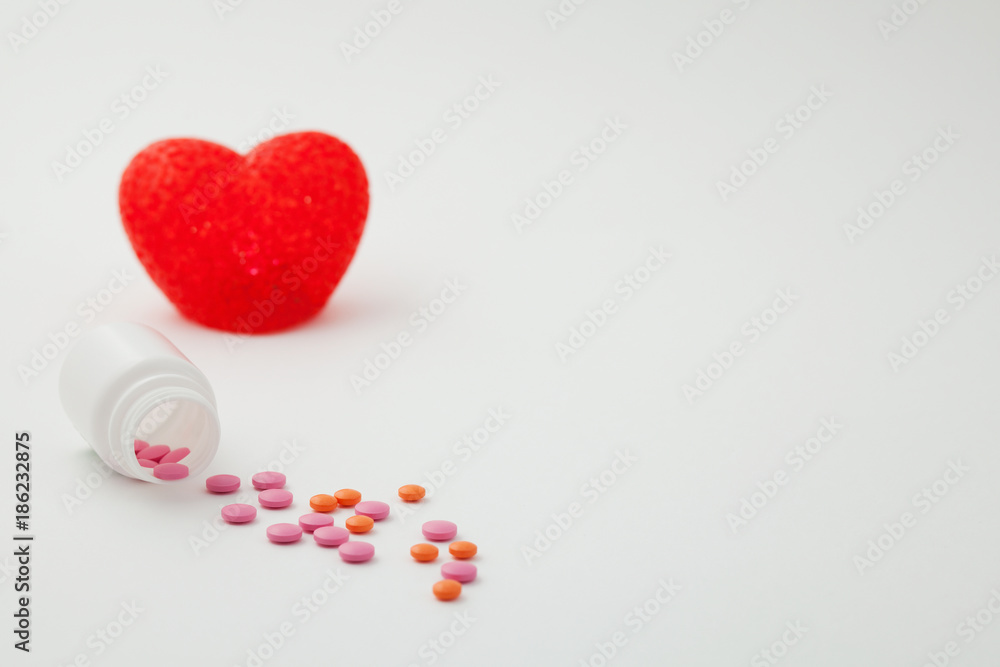 Obraz premium pills poured from a bottle and heart on a white background