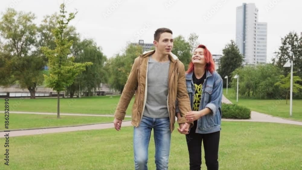 Happy man and woman holding hands and walking in the city park, slow motion Happy man and woman holding hands and walking in the city park, slow motion