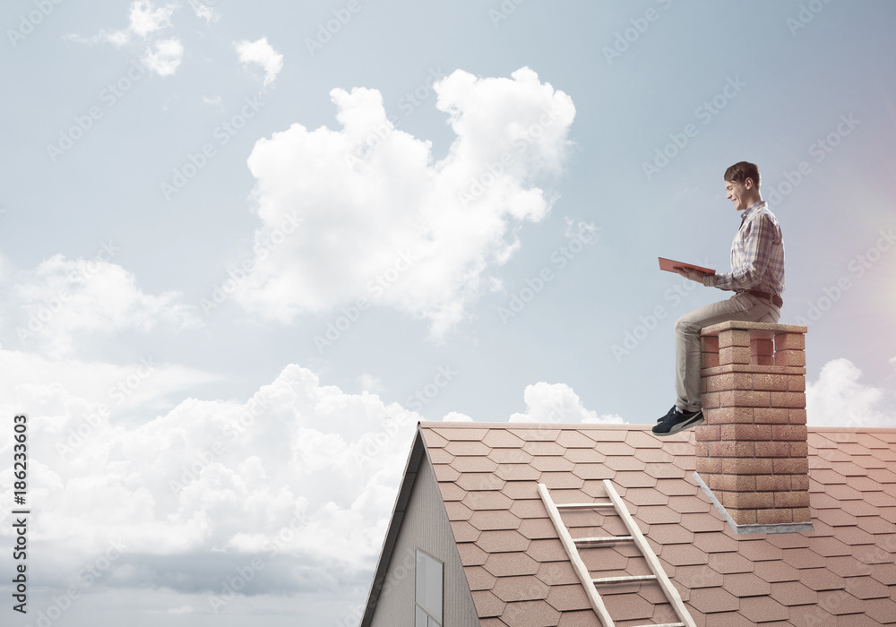 Handsome man on brick roof against cloud scape reading book Handsome man on brick roof against cloud scape reading book