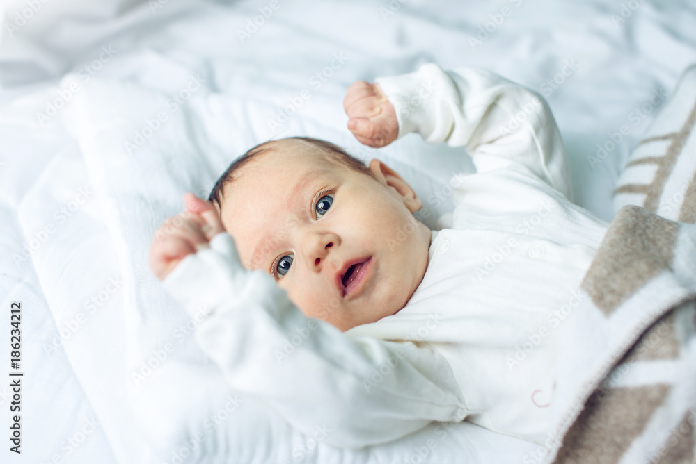 Cute funny baby lying on a white bed covered with a blanket. Concept of The tenderness of motherhood and family values Cute funny baby lying on a white bed covered with a blanket. Concept of The tenderness of motherhood and family values