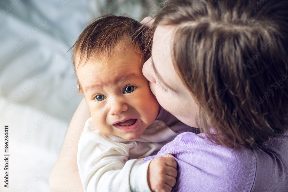 Happy caring mother holding a smiling baby boy and kisses him. Concept of the tenderness of motherhood and family values Happy caring mother holding a smiling baby boy and kisses him. Concept of the tenderness of motherhood and family values