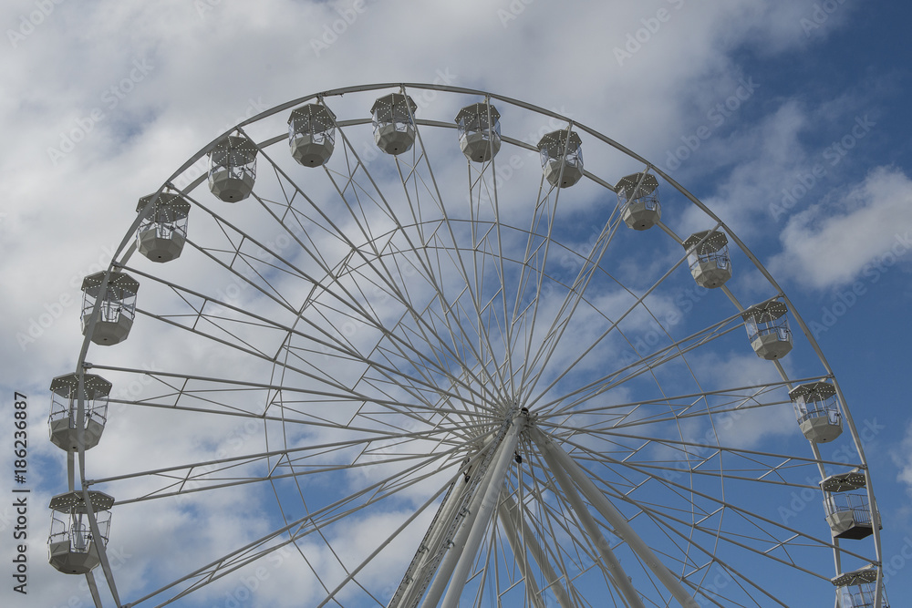 Part of a white ferris wheel on a blue sky with clouds