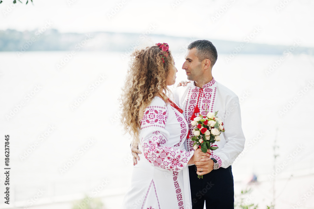 Fantastic wedding couple in ukrainian traditional embroidered clothes posing by the lake. Fantastic wedding couple in ukrainian traditional embroidered clothes posing by the lake.