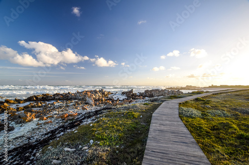 Beautiful view of a boardwalk at Cape Agulhas, South Africa's and therefore Africa's southernmost point. Beautiful bushland, rock formations and wild ocean in the background.  photo