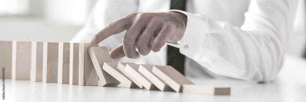 Wide cropped view of a businessman stopping domino effect - obrazy, fototapety, plakaty 