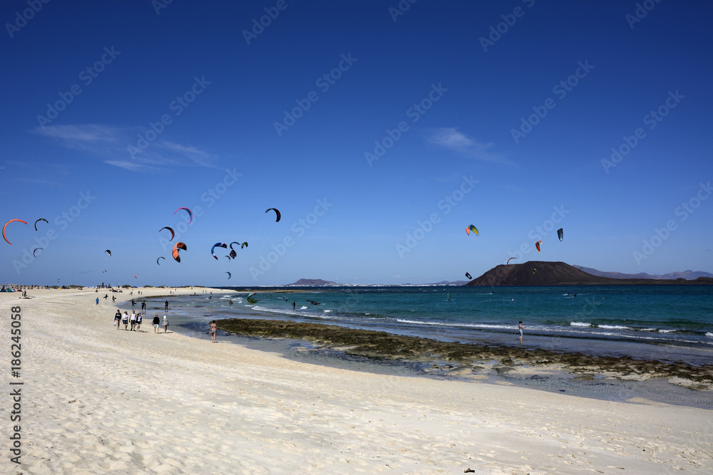 Strand Szene mit Kite Surfern und Spaziergängern.
