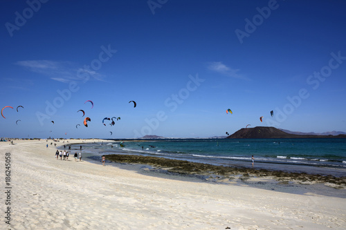 Strand Szene mit Kite Surfern und Spaziergängern.
