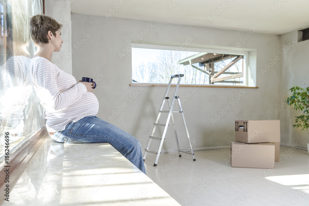 Schwangere Frau mit Tasse Tee auf der Baustelle im neuen Haus Schwangere Frau mit Tasse Tee auf der Baustelle im neuen Haus