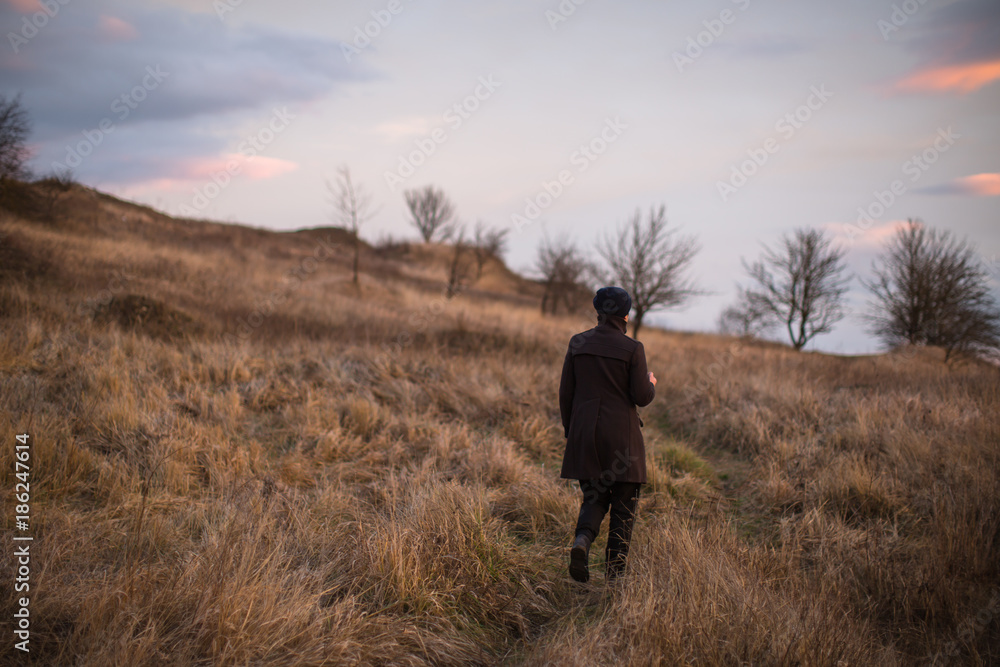 Man walking in the field with trees during sunset