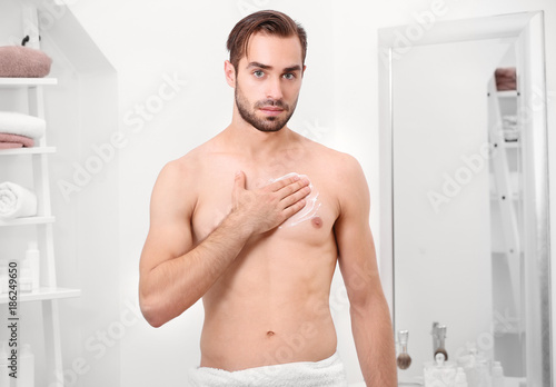 Fototapeta Naklejka Na Ścianę i Meble -  Young handsome man applying cream onto body in bathroom
