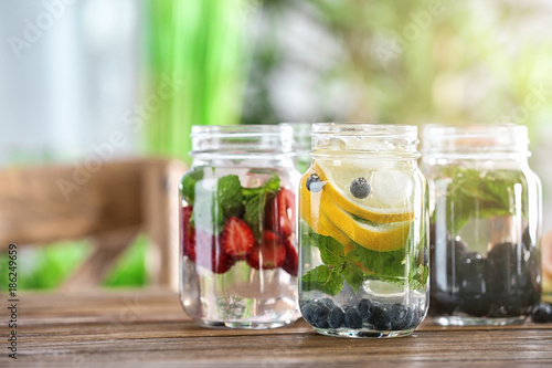 Mason jars of infused water with fruits and berries on wooden table