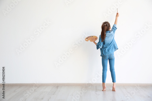Little girl painting on white wall indoors