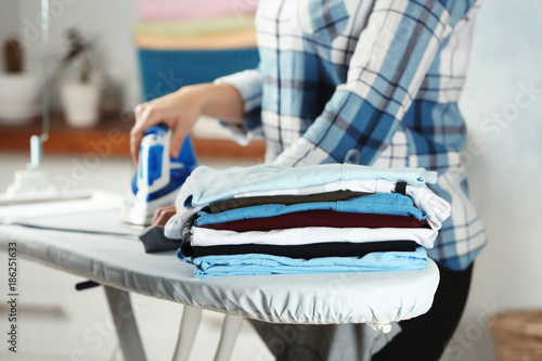 Stack of laundry and woman ironing clothes indoors