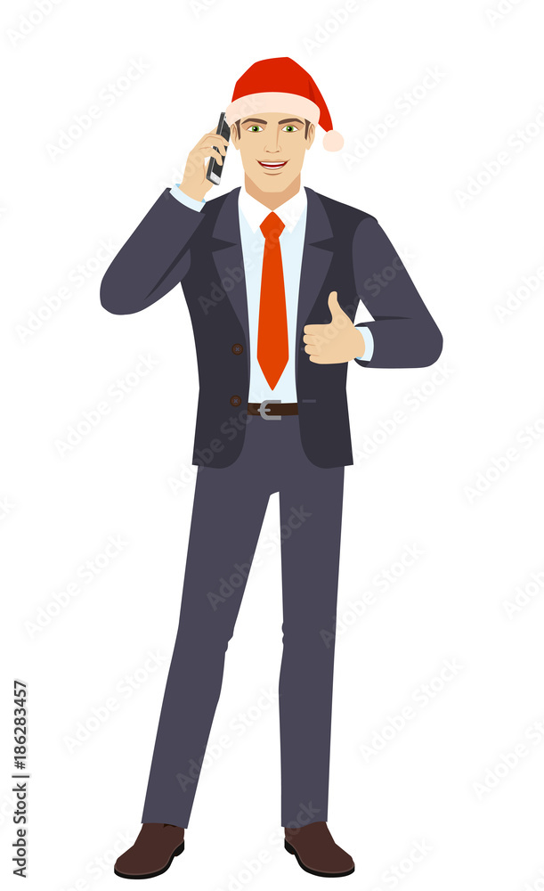 Businessman in Santa hat talking on the mobile phone and showing thumb up Businessman in Santa hat talking on the mobile phone and showing thumb up