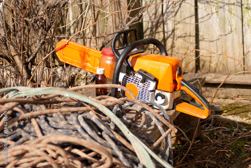 Chainsaw lies on rural bench with coils of ropes Chainsaw lies on rural bench with coils of ropes